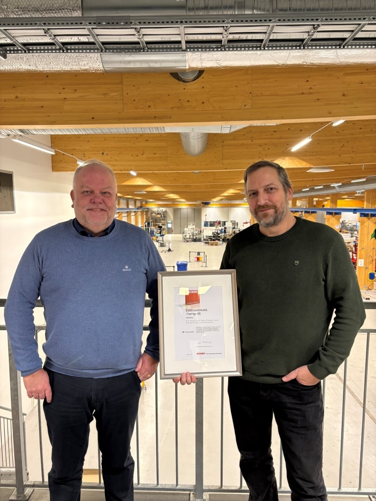 Två män står i en verkstadshall, en av männen håller i en ram